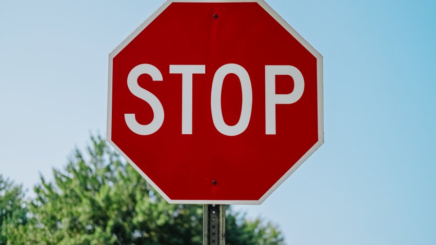 Close-up of stop sign at intersection set against sky with top section of trees in background